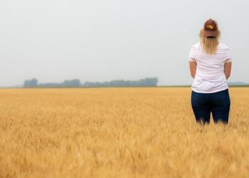 Female student standing in a wheat field with a backwards Golden Eagle hat on