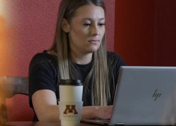 Student at a computer with UMCrookston mug with faded in pics of females with a laptop and tablet in a wheat field