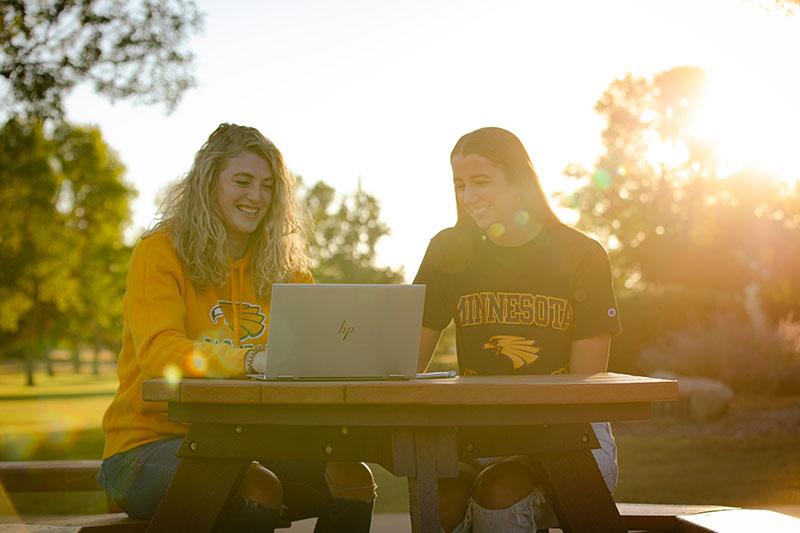 Two students early in the morning sitting at a table on the Campus Mall with their laptops